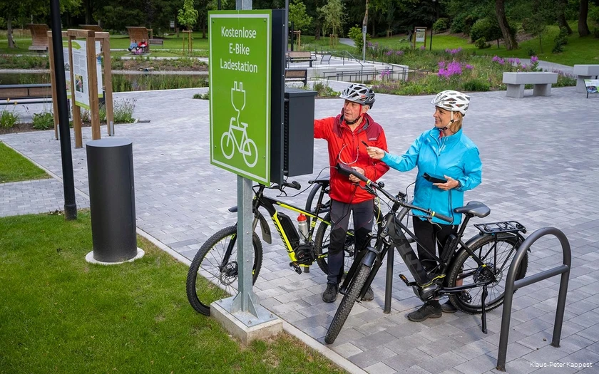 Zwei Radfahrer, aktivieren die Ladefunktion an einer kostenlosen E-Bike Ladestation.