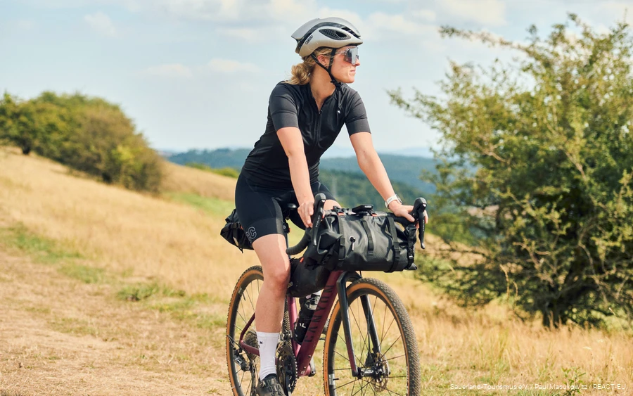 Eine Gravelbikerin mit Bikepackingtaschen fährt durch das Sauerland.