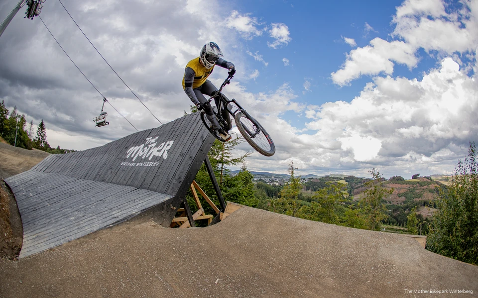 Mountainbiker springt aus einer Holzanliegerkurve einer sogenannten Sharkfin