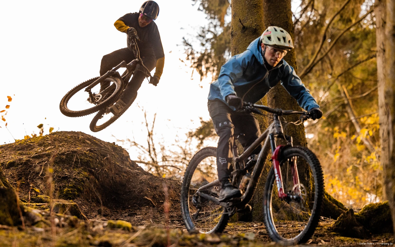 Zwei Mountainbiker fahren im Trailpark Winterberg, der hintere nimmt gerade einen Sprung.