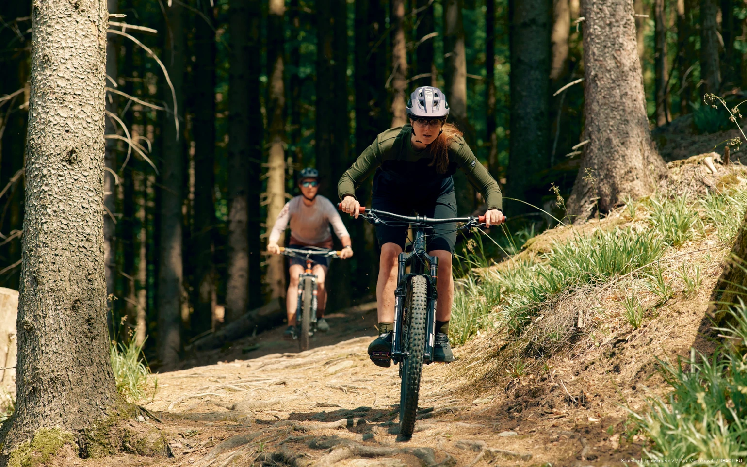2 Mountainbikerinnen fahren Wurzelpfad im Wald herunter